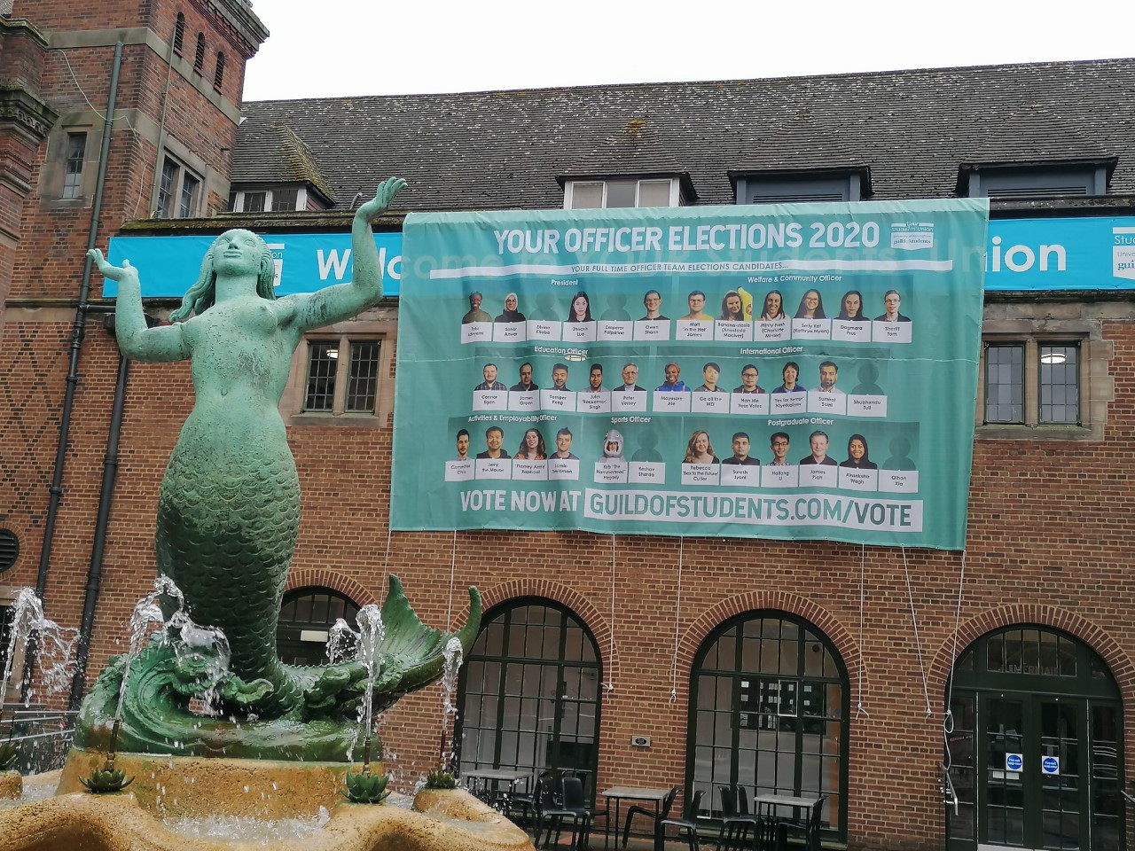 A banner showing the Guild Elections candidates behind the mermaid fountain at the Birmingham Guild of Students